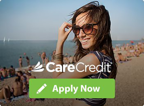 A woman with sunglasses on the beach smiling for carecredit.